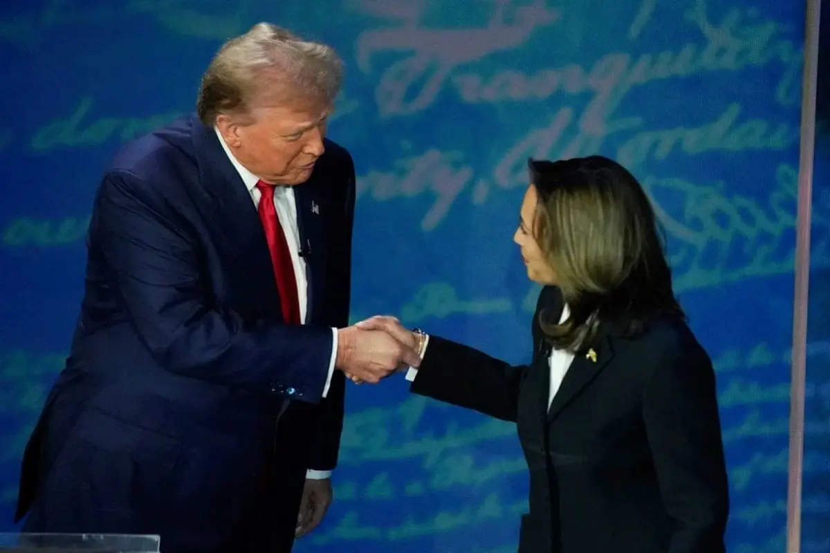 Donald Trump and Kamala Harris shaking hands at the 2024 U.S. Presidential debate stage against a blue backdrop with script text.