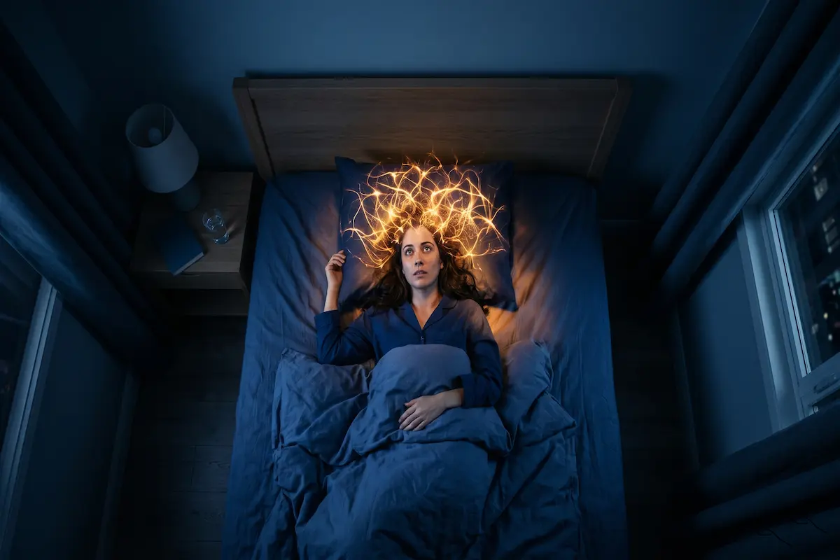 Person in dark bed with a glowing golden web of energy around their head, symbolizing racing thoughts.